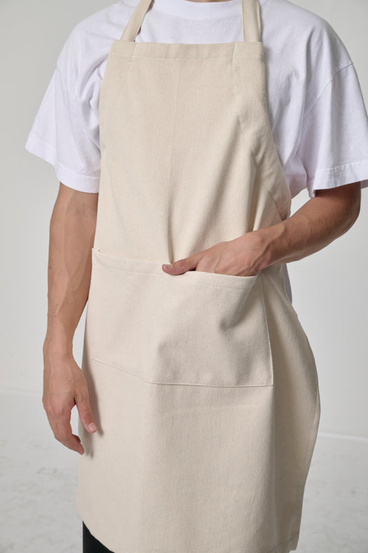 Close-up of a person wearing a light beige Natural adjustable apron, hand in front pocket to show depth.