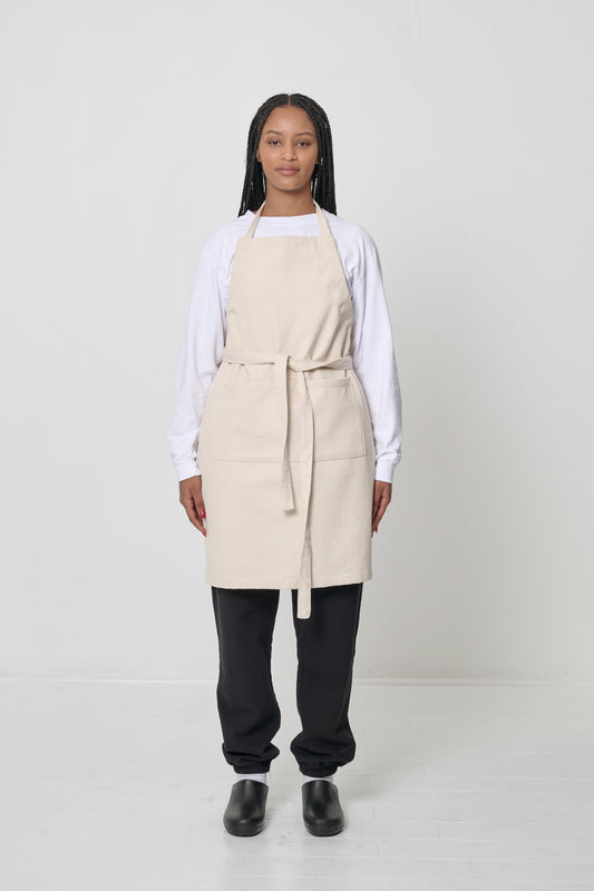 Front view of a person in an Adjustable Apron in Natural, with straps long enough to tie in the front.