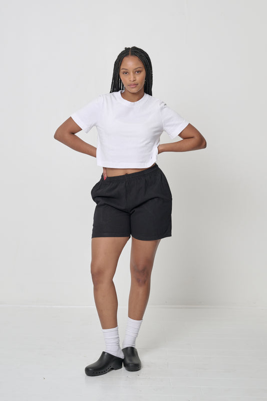 Woman wearing White Baby Trash Tee, which is cropped above her navel; hands on her waist.