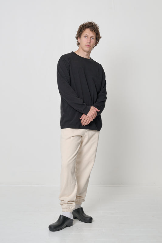 Full length of a man in a Black Long Sleeve Trash Tee, hands crossed, highlighting relaxed fabric drape.