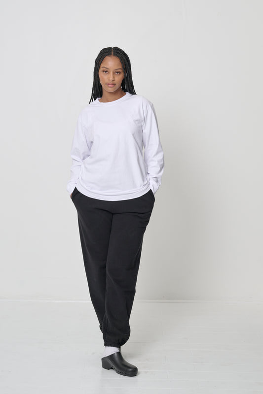 Woman in a White Long Sleeve Trash Tee, hands in her sweatpants pocket, showcasing fabric drape.