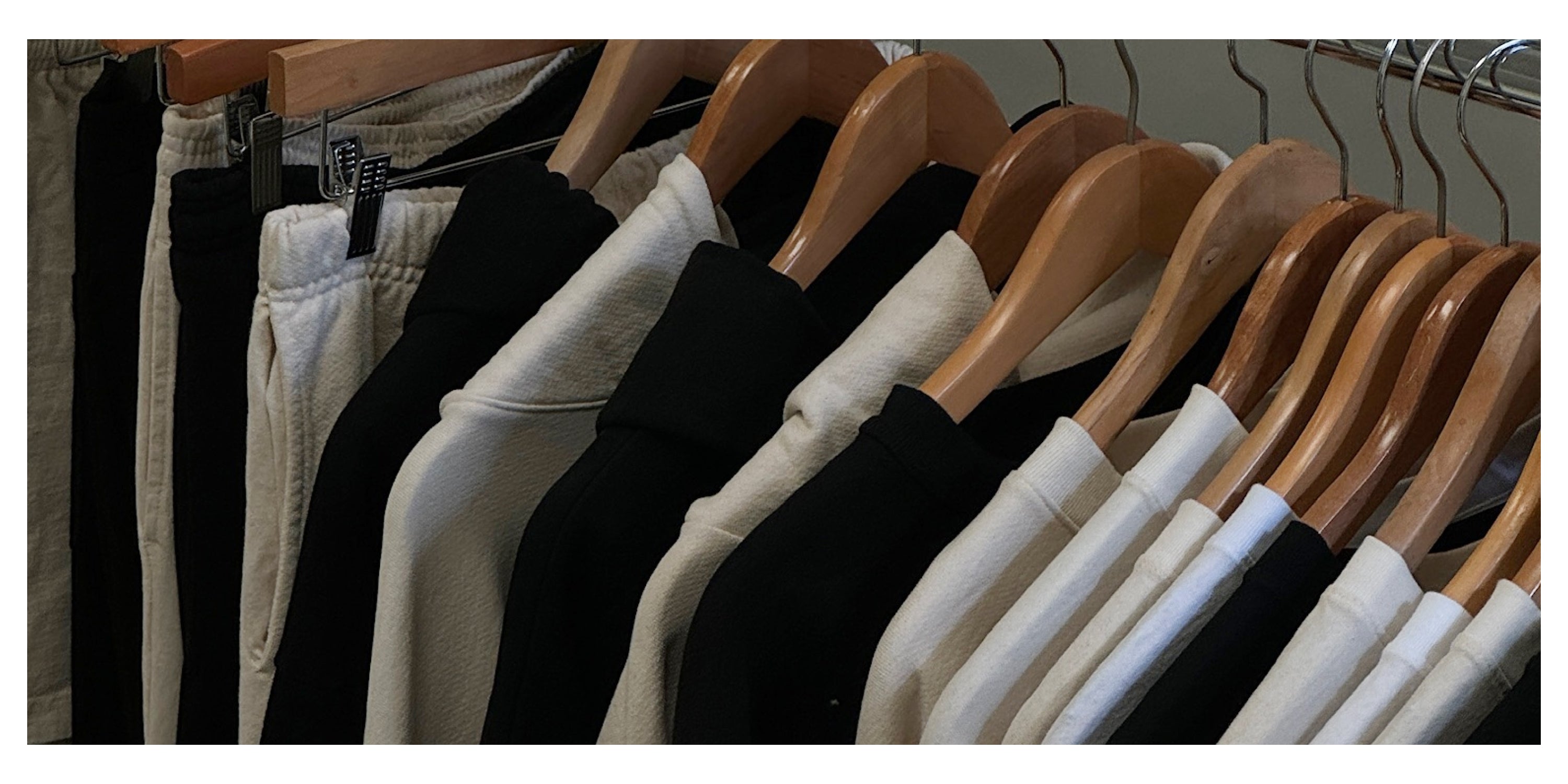 A clothing rack featuring neatly arranged black and white loungewear garments on wooden hangers, reflecting sustainable and minimalist fashion.