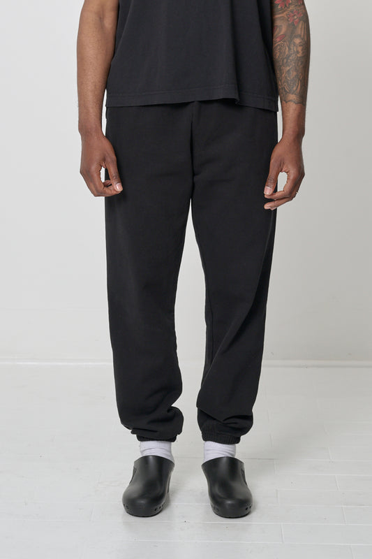 Front view: 6'2" person in size L Black Trash Sweatpants, relaxed fit, slight bunching at the ankles.