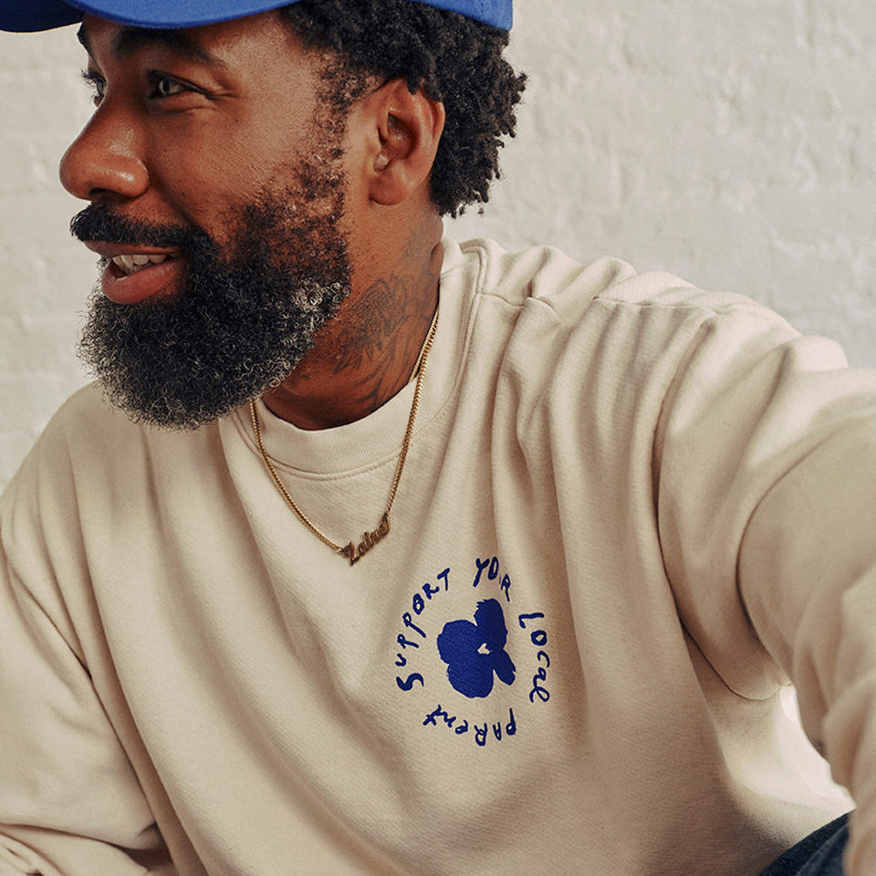 Man wearing a Trash Crewneck in Scour with a blue flower design and text that says "Support Your Local Parent".