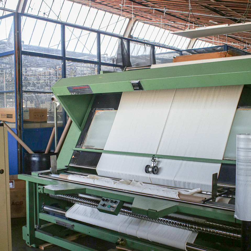 Large green textile machine with fabric in a factory setting.