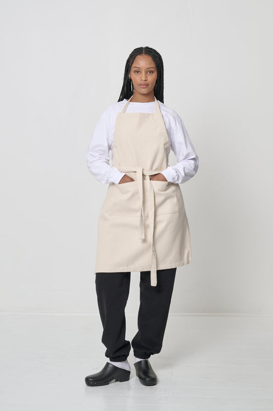 Natural Adjustable Apron on a woman, covering chest to knees, hands in large front pocket.