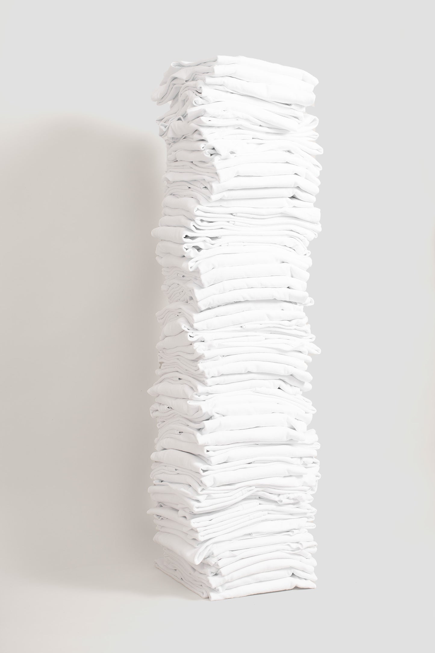 Stack of sixty folded Boxier Trash Tees in White against a plain background.