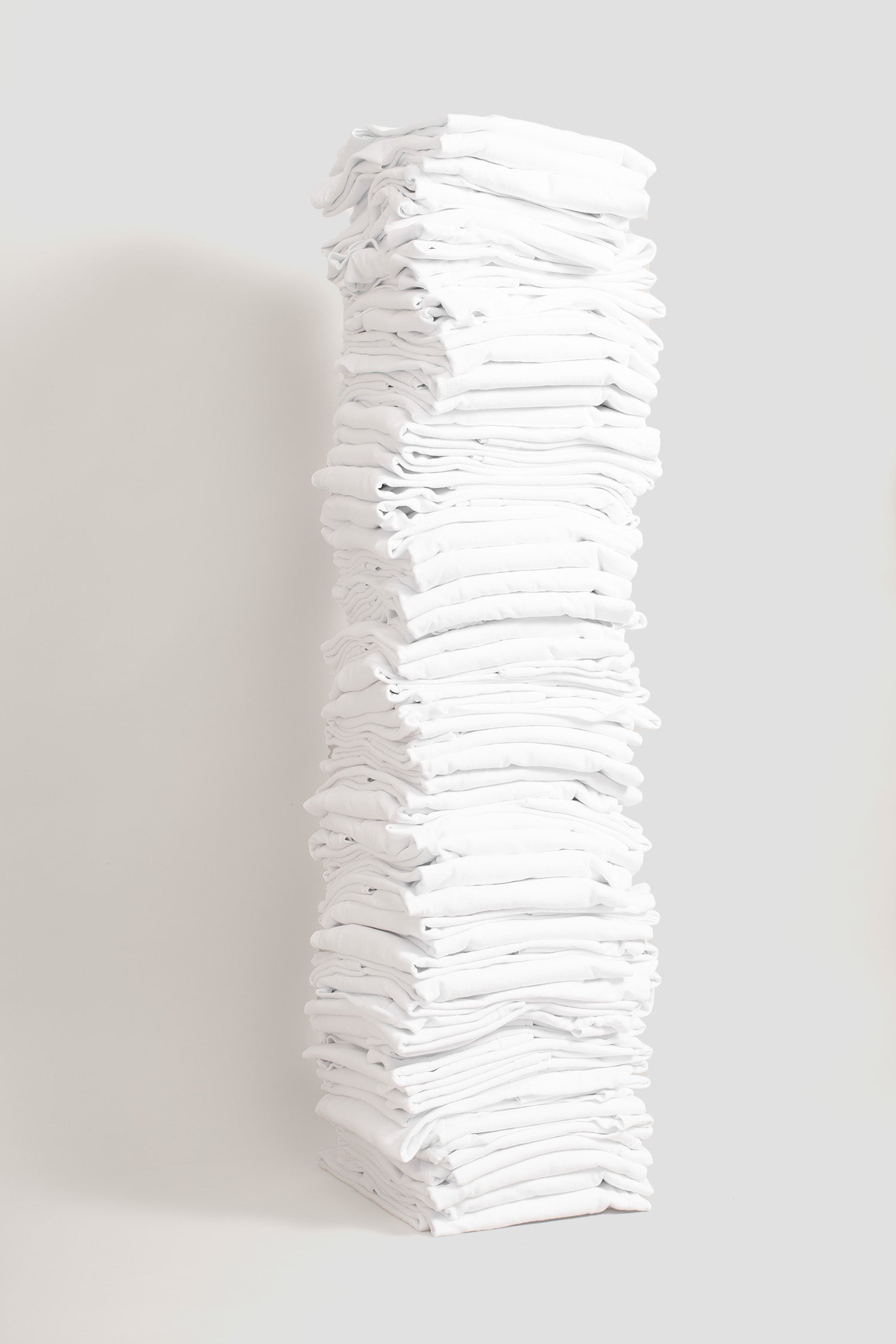 Stack of sixty folded Boxier Trash Tees in White against a plain background.