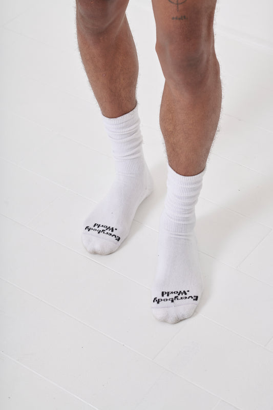 Overhead view of White Squishy Socks, branded 'Everybody.World' in black, at the toe, shown on a person's lower legs.