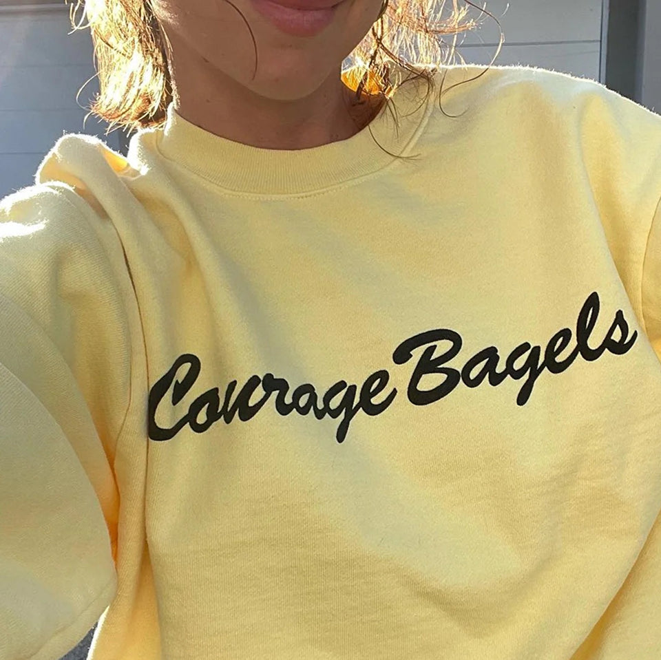 Custom Trash Crewneck in French Butter with 'Courage Bagels' text worn by a person.