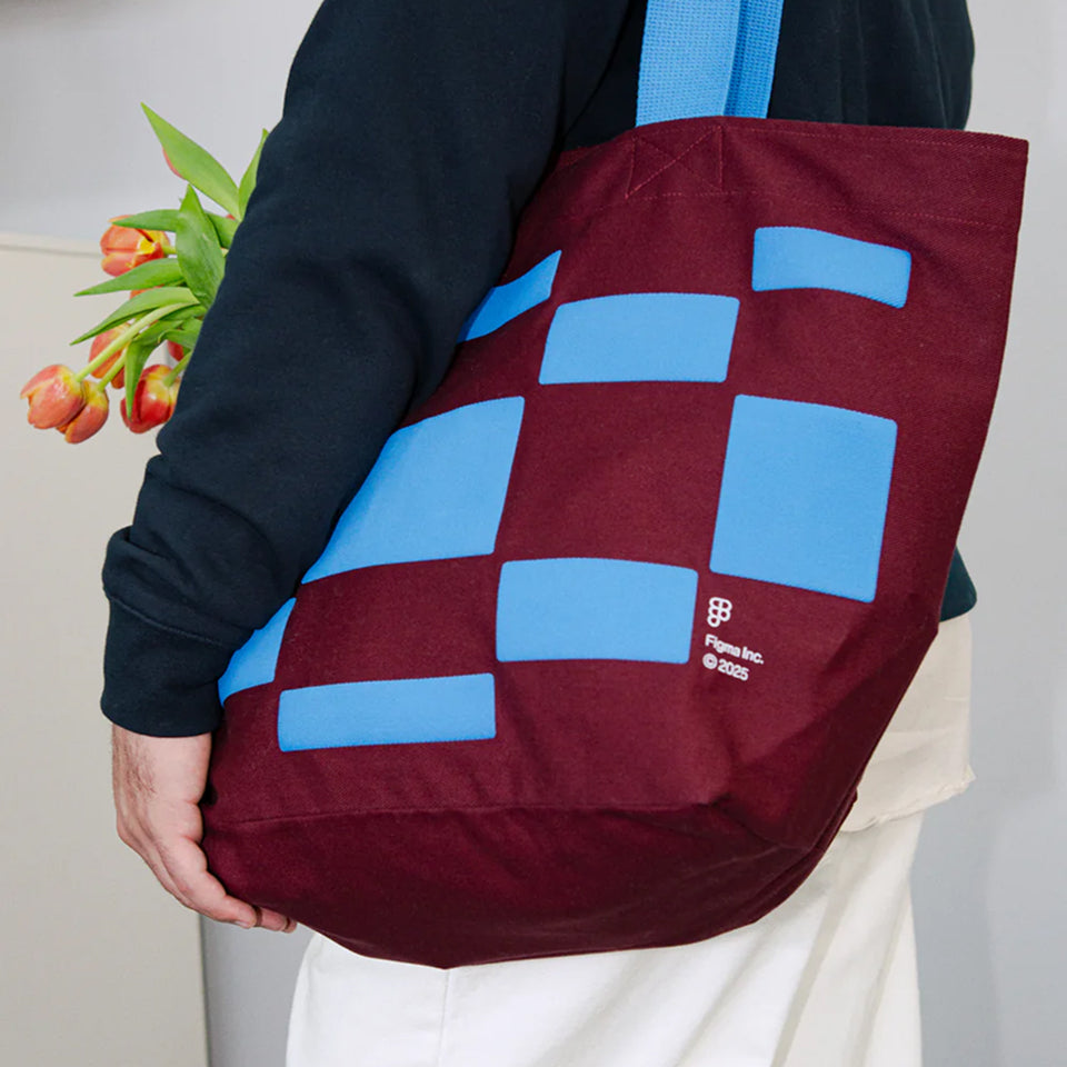 Person holding a custom maroon and blue Classic Tote with blue geometric patterns that is holding tulips, wearing a black sweatshirt and white pants.