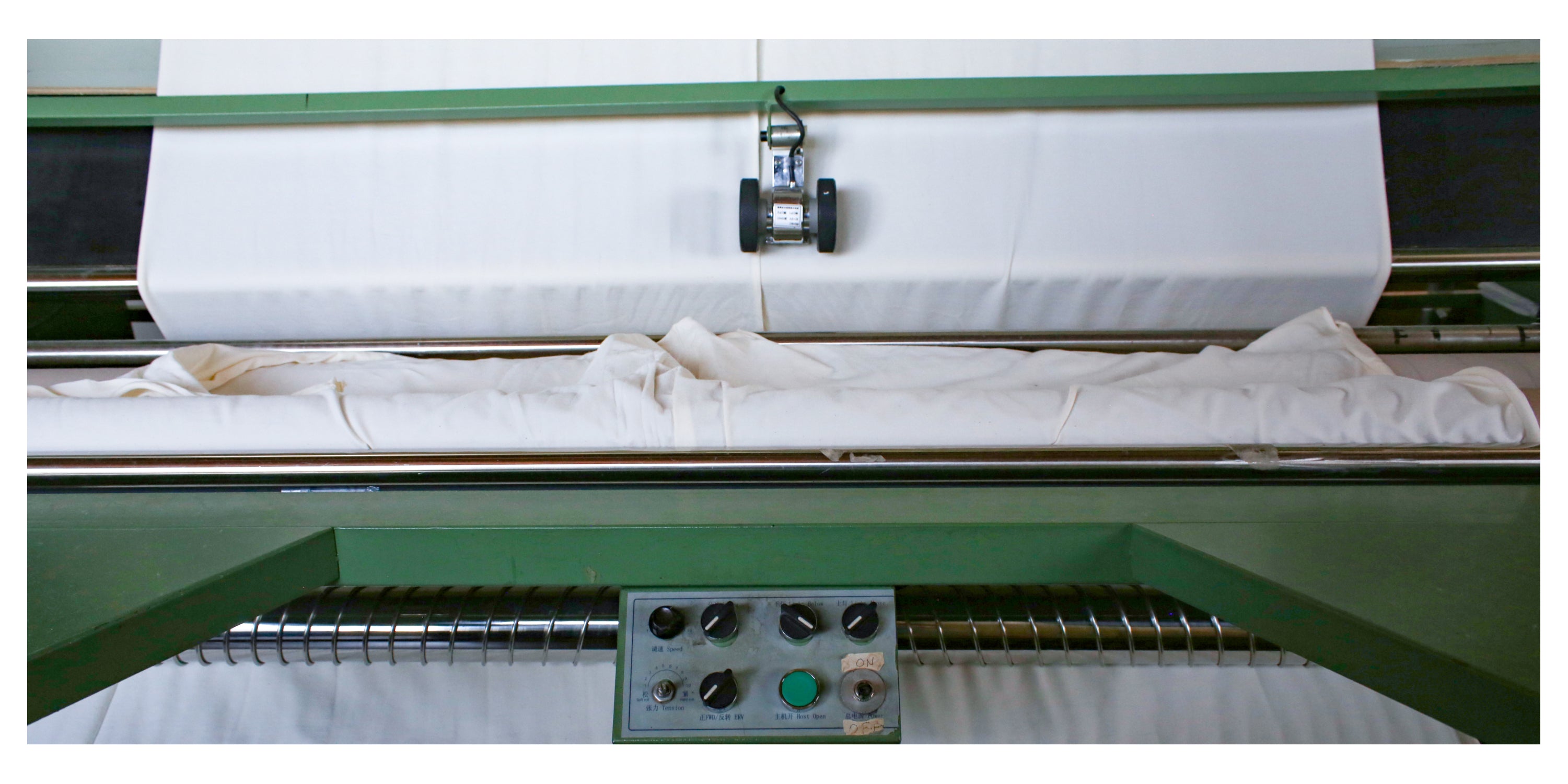 Close up on part of a green textile machine with white fabric.