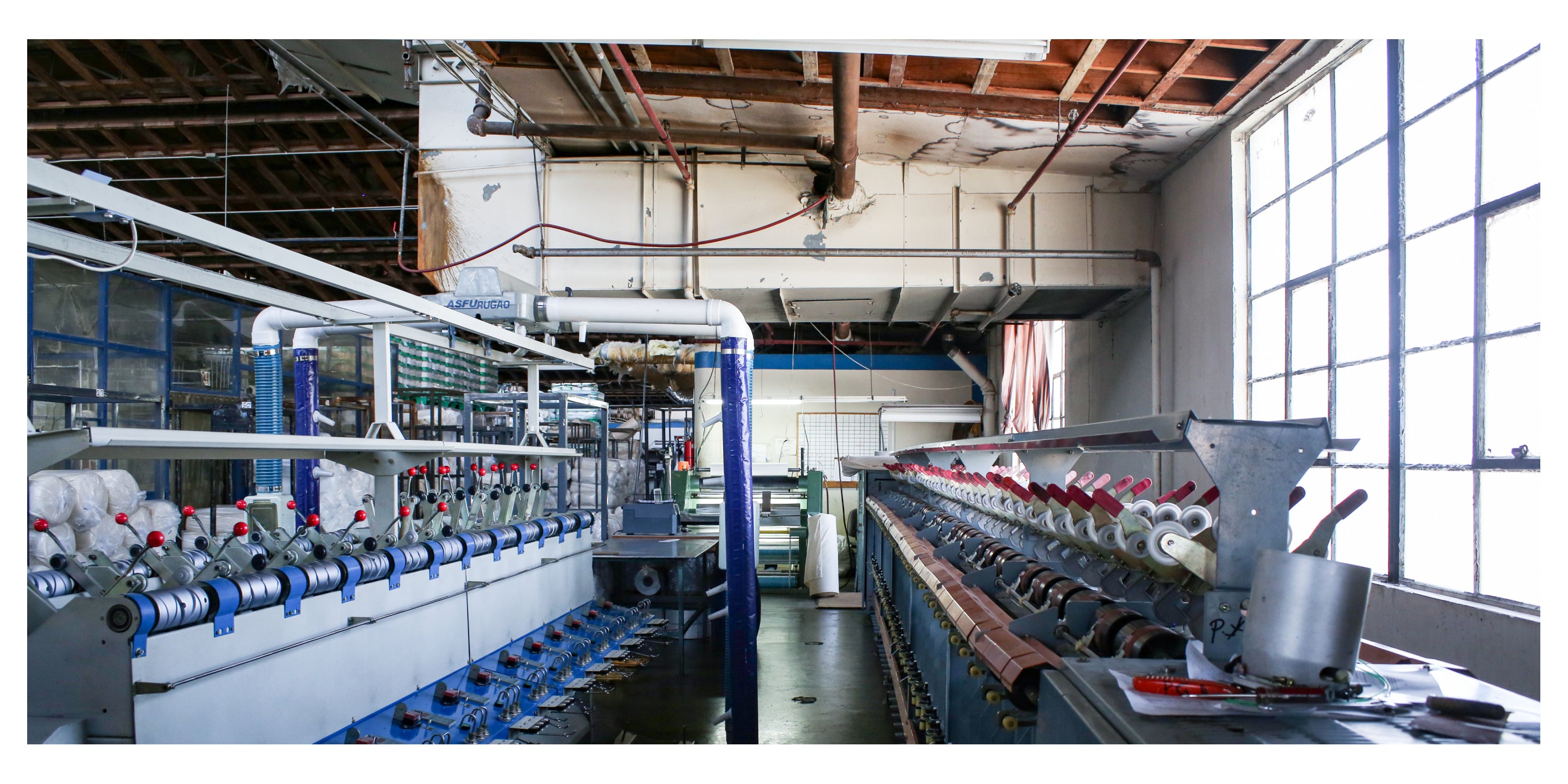 Industrial textile machinery in a factory setting with large windows.