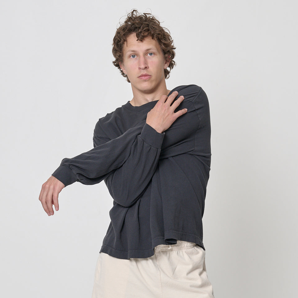 Person wearing a Boxier Long Sleeve Trash Tee in Slate with their arms crossed, and Apartment Pants in Scour.