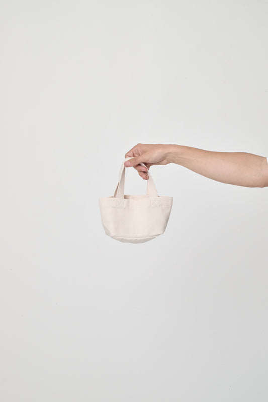 Mini Tote in Natural, held in a person's hand, showing stitching and web straps.