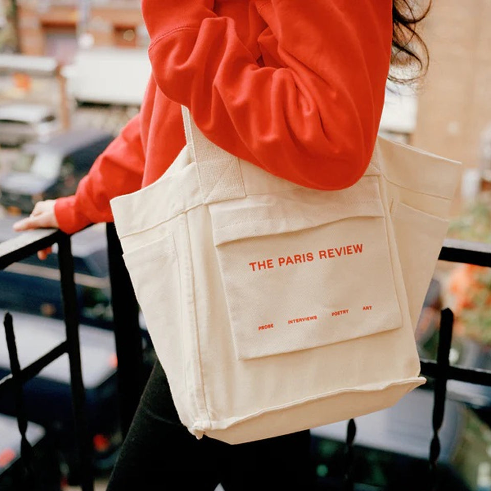 Person holding a custom Tote Bag in Natural with 'The Paris Review' branding.