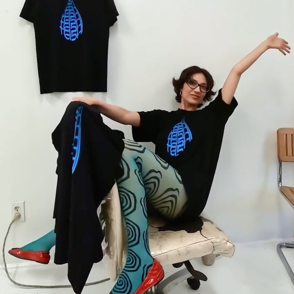 Musician Tei Shi wearing a custom Boxier Trash Tee blue graphic design, sitting on a chair with a white wall background.
