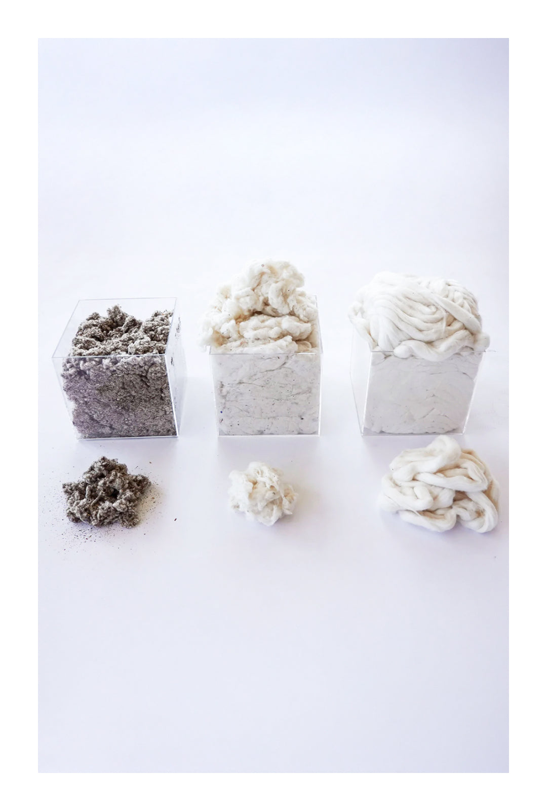 Three transparent containers filled with varying stages of recycled cotton material—gray dust, loose fibers, and compacted cotton—against a white background.