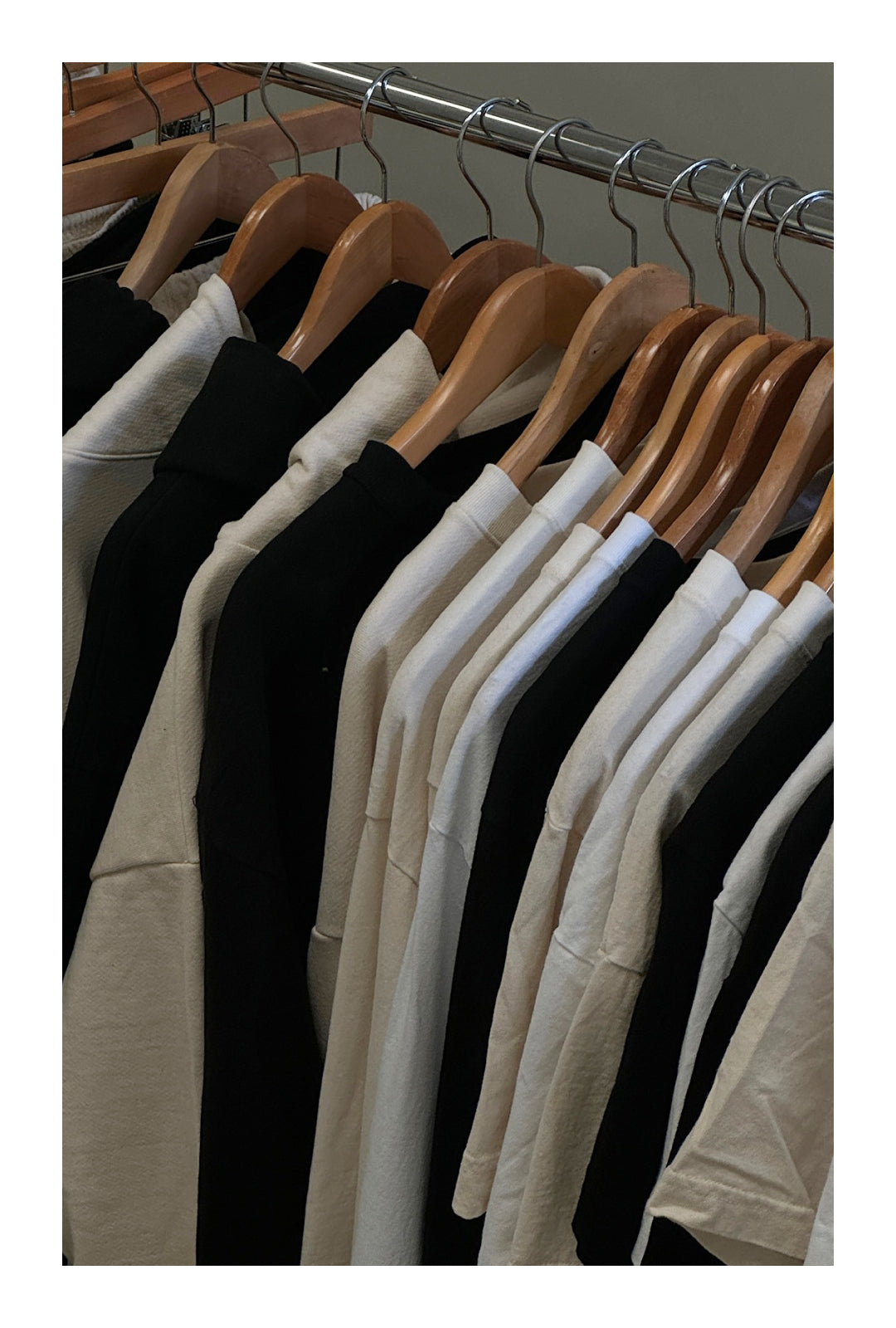 A clothing rack featuring neatly arranged black and white loungewear garments on wooden hangers, reflecting sustainable and minimalist fashion.