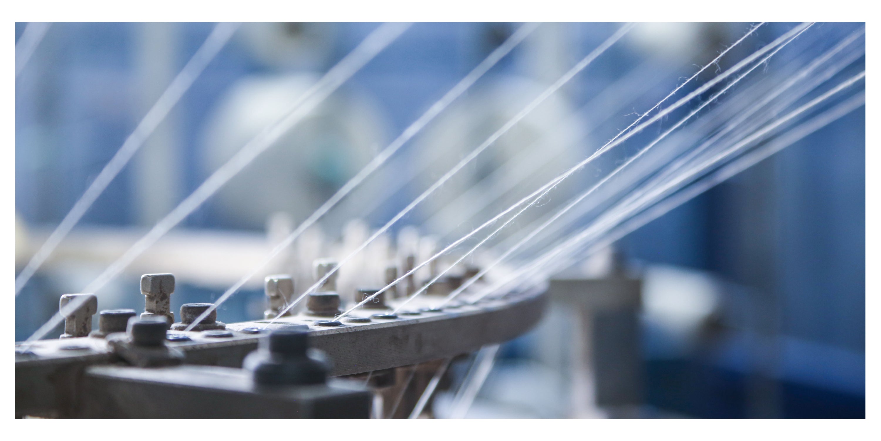 Close-up of a cotton threads strung through a knitting machine.