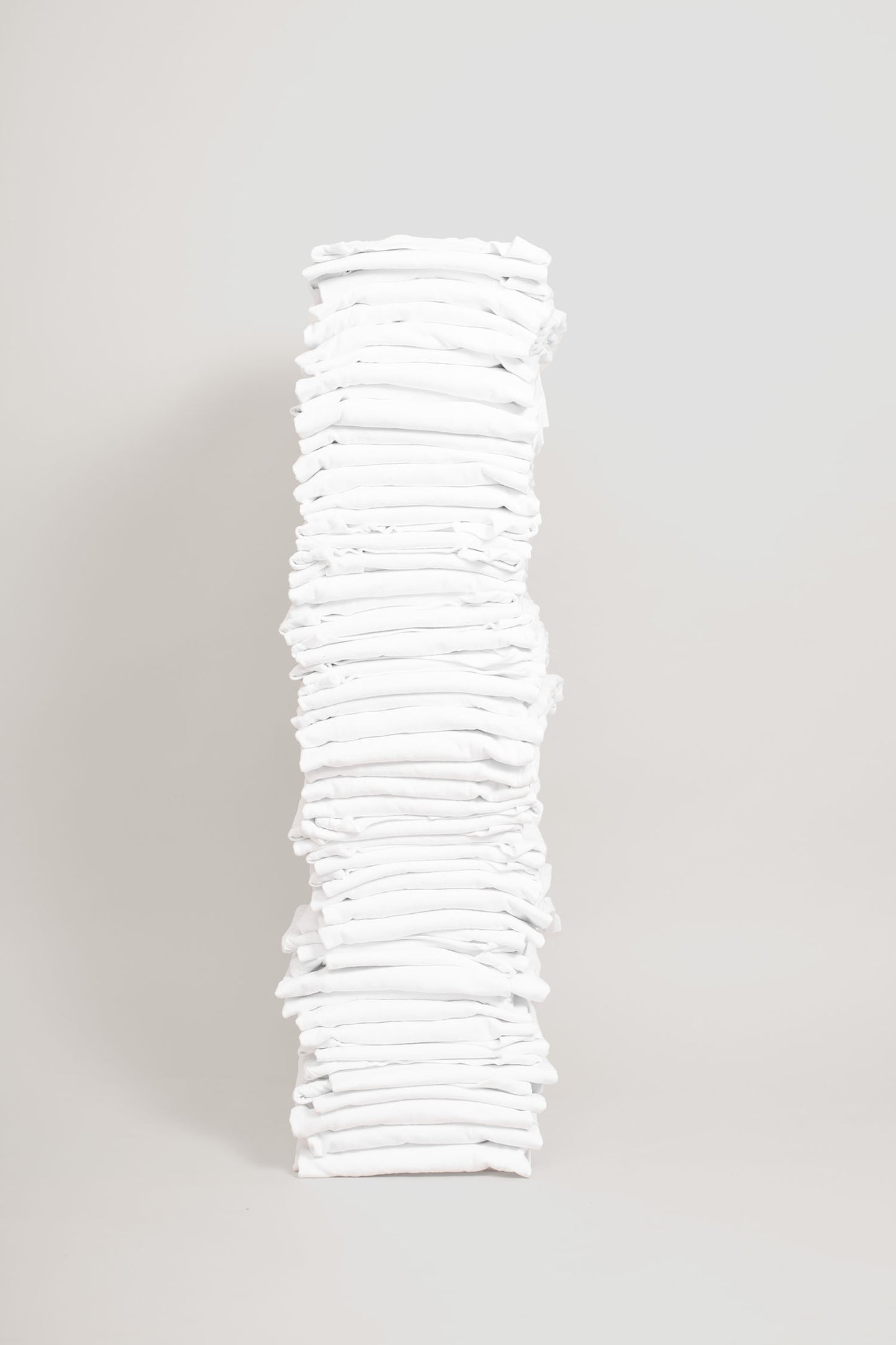 Stack of fifty folded Long Sleeve Trash Tees in White against a blank backdrop.