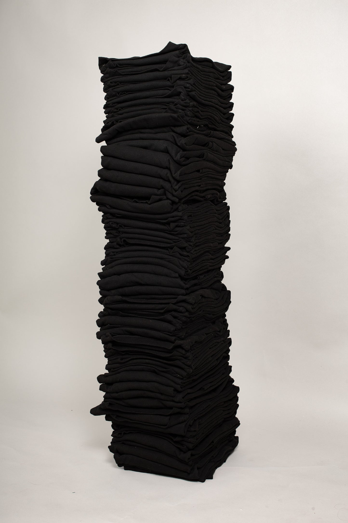 Stack of sixty folded Short Sleeve Trash Tees in Black against a plain background.