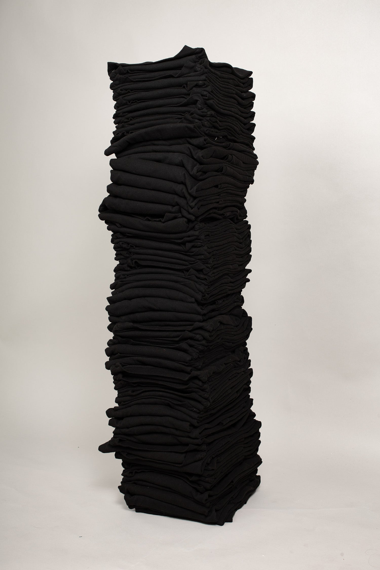 Stack of sixty folded Short Sleeve Trash Tees in Black against a plain background.