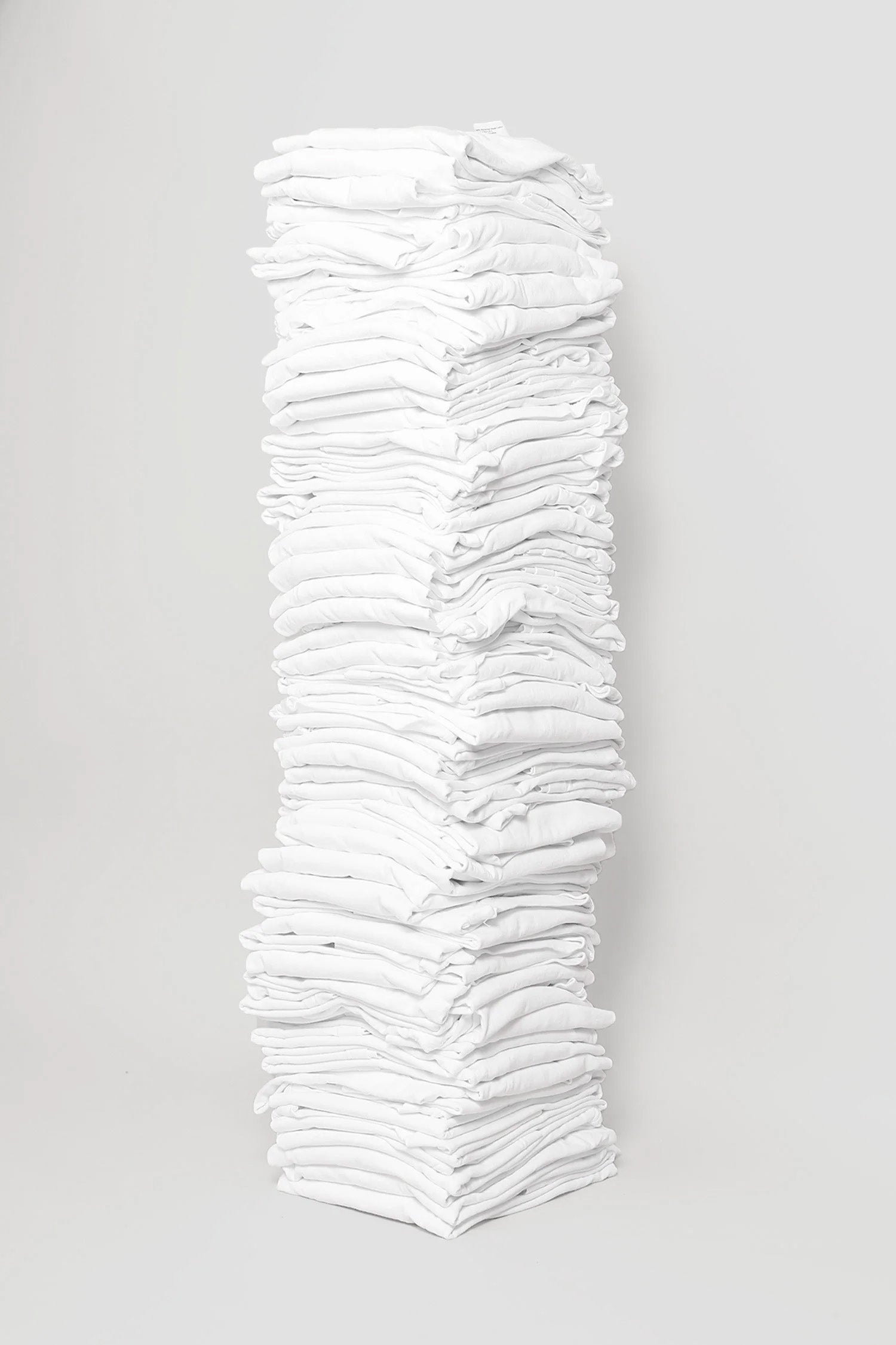 Stack of sixty folded Short Sleeve Trash Tees in White against a plain background.