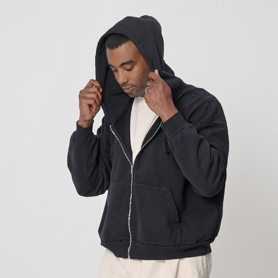 Man wearing a Trash Zip Up Hoodie in Black against a plain background with the hood pulled up.