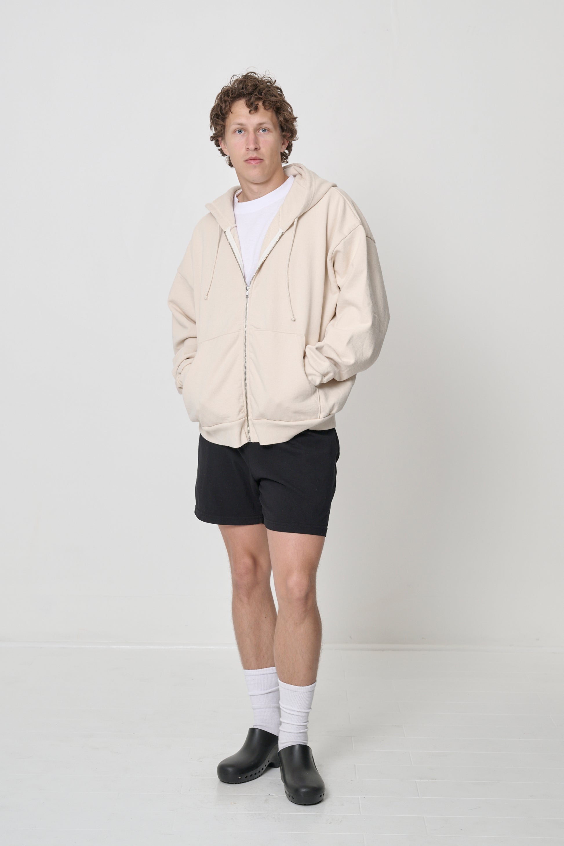 Front view: man wearing a zipped up Scour Trash Zip Up Hoodie with hands in the kangaroo pockets.