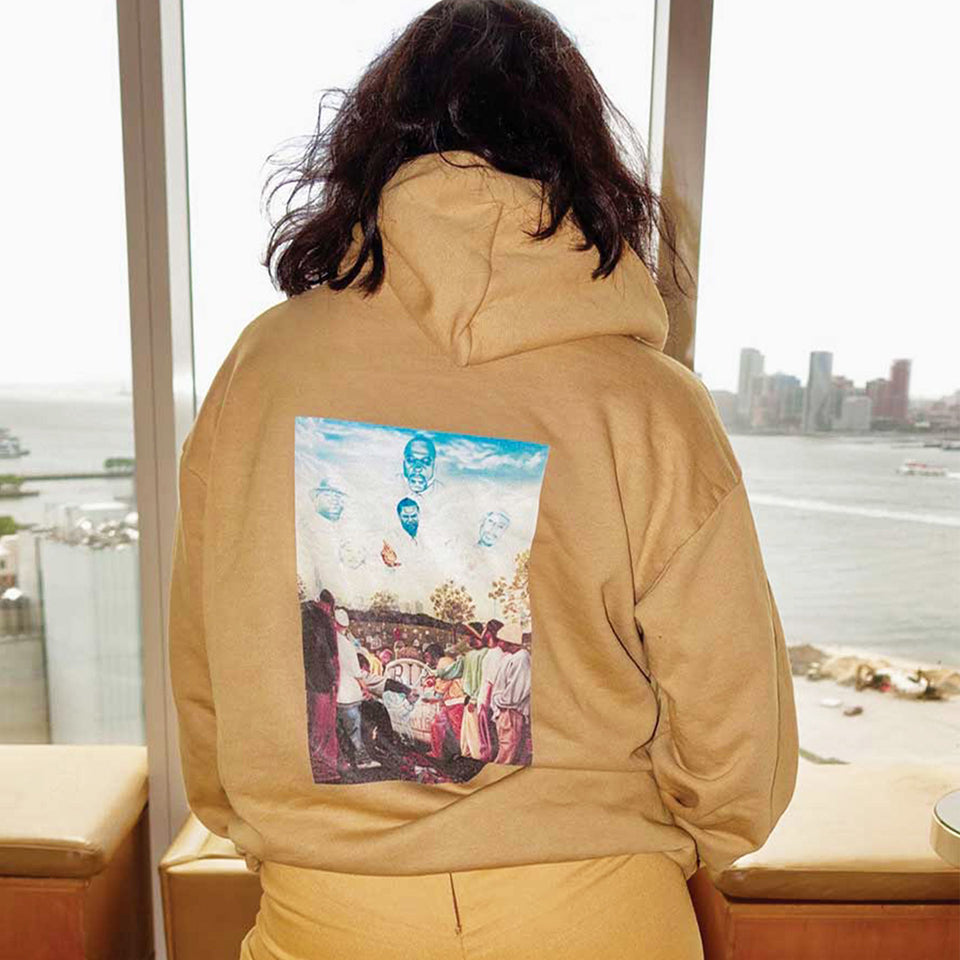 Person wearing a custom yellow color Trash Hoodie with a colorful graphic on the back, standing in a room with large windows overlooking a waterfront.