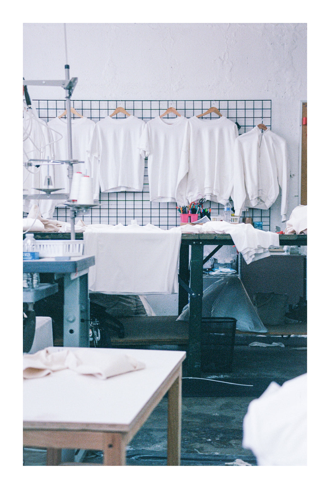 Everybody.World T-shirts and sweatshirts in pfd hanging on a wall grid with sewing machine parts in the foreground.