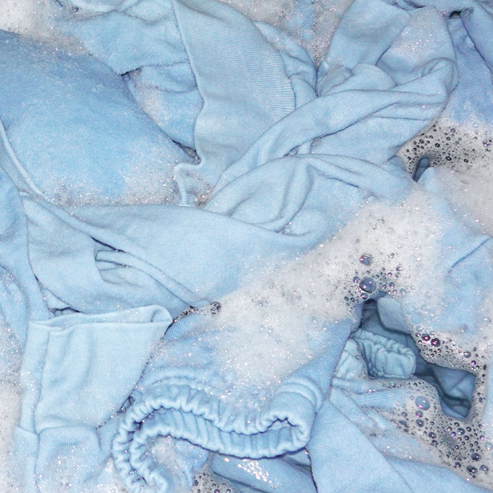 Close up of light blue clothing in a washing machine with bubbles.